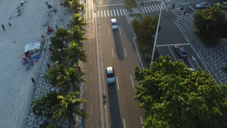 Cars-on-busy-avenue-at-Rio-de-Janeiro,-sunset-time-big-shadows-golden-hour-near-the-beach----drone-aerial-shot