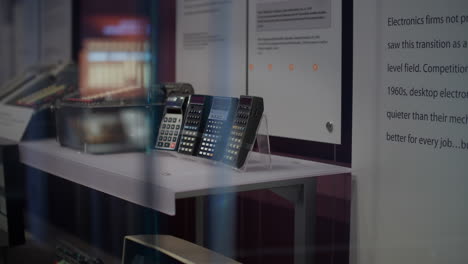 Computermuseum,-Auf-Weißem-Tisch-Sind-Taschenrechner-Ausgestellt,-Dahinter-Beschreibungen-Und-Deren-Geschichte