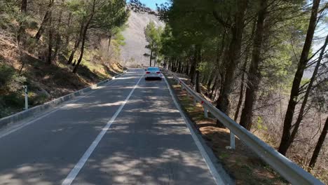 Coche-Sedán-Blanco-Conduciendo-Por-Una-Sinuosa-Carretera-De-Montaña-Con-árboles-A-Los-Lados