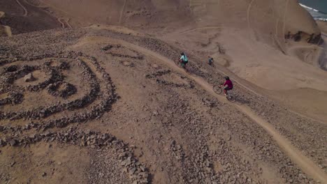 Tracking-Shot-Of-Cyclists-Riding-On-High-Sandy-Peak-At-Morro-Solar,-Lima
