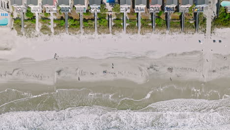 Aerial-top-down-shot-of-sandy-beach-with-walking-people-and-reaching-waves-at-surfside-beach-in-South-Carolina