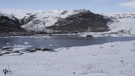Rotierende-Luftaufnahme-Eines-Zugefrorenen-Sees,-Umgeben-Von-Isländischen-Schneebedeckten-Bergen
