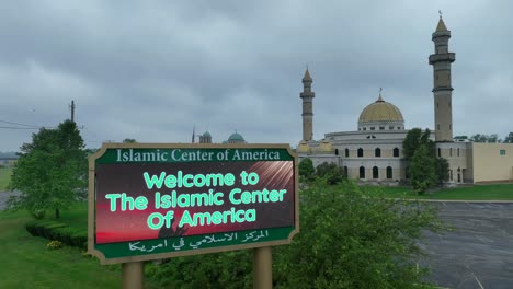 Vista-Aérea-Que-Muestra-La-Bienvenida-Al-Cartel-Digital-Del-Centro-Islámico-De-América-Y-Al-Edificio-De-La-Mezquita-En-Segundo-Plano-Durante-El-Día-Nublado