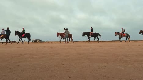 Seitliche-Kamerafahrt-Einer-Pferdekarawane,-Die-Kutschen-Zieht,-Und-Touristen-Zu-Pferd,-Die-Die-Wüste-Djerba-In-Tunesien-Durchqueren