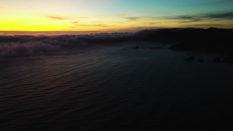 Drone-shot-tilting-over-the-ocean,-revealing-Sea-fret-moving-over-the-costline