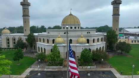 Ascending-drone-shot-of-american-flag-in-front-of-beautiful-Islamic-Center-of-America-during-cloudy-day---Rising-establishing-shot
