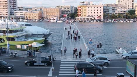 Zadar-pedestrian-bridge-with-people,-street-traffic-with-crossing,-city-buildings,-Croatia-in-summer-evening