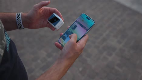 Overhead-Shot-Of-Adult-Scrolling-Through-Photos-On-Smartphone-In-On-Hand-Whilst-Holding-Insta360-Go-3-In-The-Other