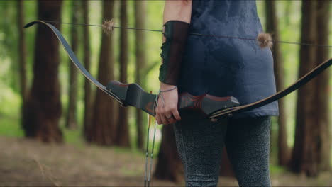 Archery-girl-picks-an-arrow-from-the-ground-and-pulls-her-bow-in-a-forest-tilt-medium-shot
