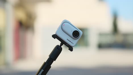 Insta360-Go-3-Auf-Einem-Selfie-Stick-Kommt-In-Die-Aufnahme-Mit-Hellem-Bokeh-Hintergrund