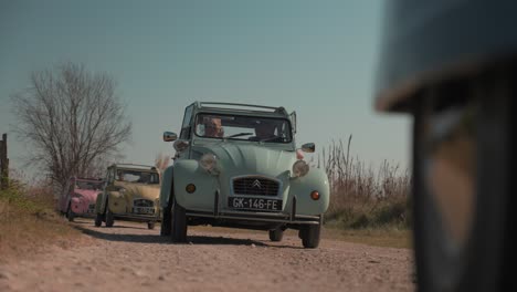 A-convoy-of-retro-Citroen-CV-2-cars-driving-slowly-along-a-dirt-road