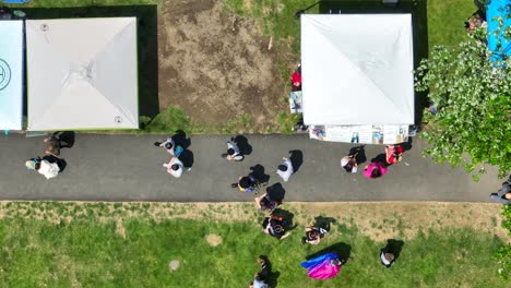 Aerial-top-down-shot-of-walking-people-on-path-in-park-beside-stall-at-LGBT-Pride-Festival