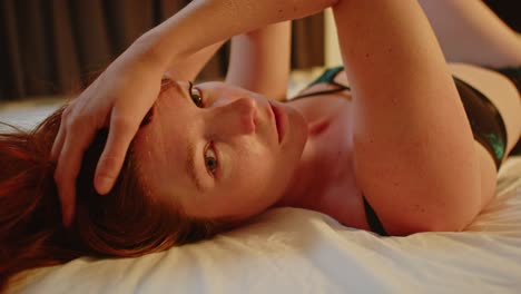 A-beautiful-woman-with-red-hair-wearing-lingerie-lies-in-bed,-she-looks-enticingly-to-camera-and-seduces-the-viewer