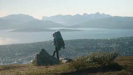 Beautiful-Hiker-Girl-with-Heavy-Backpack,-Standing-on-a-Cliff-and-Enjoying-the-Spectacular-View-of-Tromsø,-Sunny-Summer-Day-in-Norway