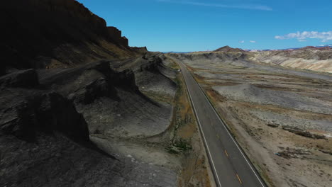 Drone-shot-tilting-over-a-car-on-a-road,-in-middle-of-rock-formations-in-southwest-USA
