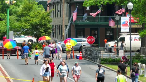Drone-slow-motion-showing-many-people-celebrating-LGBTQ-Pride-Festival-during-sunny-day---Cars-on-road-and-waving-american-flag-in-background
