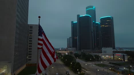 Bandera-Americana-Ondeando-Frente-Al-Centro-Renacentista-Y-La-Sede-General-De-Motores-En-Detroit,-Michigan