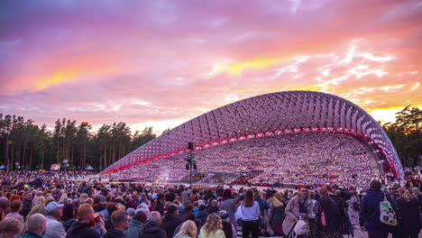 Modern-oval-shaped-auditorium-full-of-people-with-pink-and-gold-sky-at-sunset