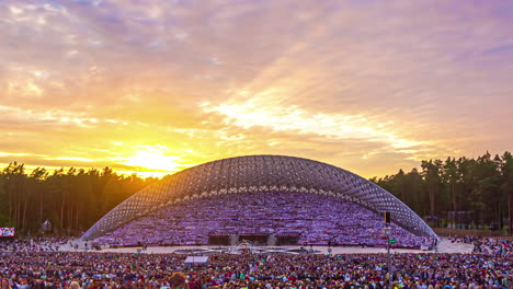 Auditorio-Moderno-De-Forma-Ovalada-Lleno-De-Gente-Con-El-Sol-Dorado-Al-Atardecer