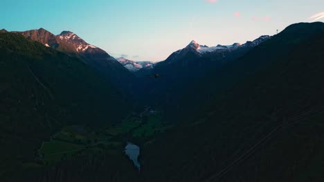 Rastreando-Un-Dron-Sobre-Un-Valle-Durante-La-Puesta-De-Sol-Con-Picos-Nevados-Al-Fondo,-Kitzsteinhorn-En-Austria
