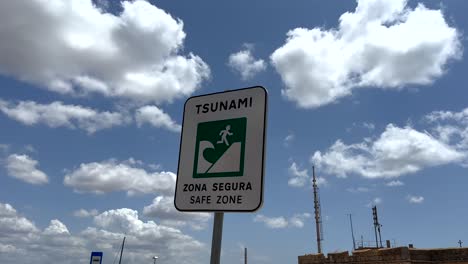 Close-up-shot-of-Tsunami-Sign-in-Safe-Zone-against-blue-sky-and-clouds-at-ocean-in-Portugal