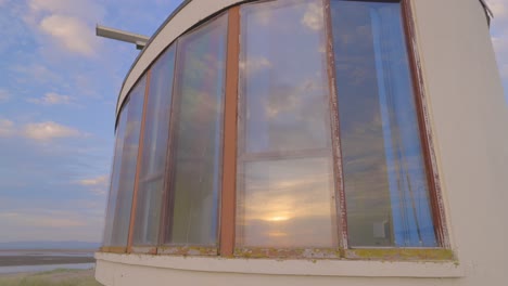 Pan-across-curved-beach-structure-with-sunset-reflection-in-windows-in-slow-motion-at-the-old-maritime-college-building,-Fleetwood,-Lancashire,-England,-UK