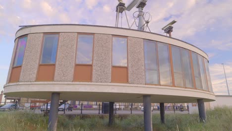 Rise-up-showing-curved-building-on-stilts-with-radar-equipment-on-roof-at-beach-in-slow-motion-at-the-old-maritime-college-building,-Fleetwood,-Lancashire,-England,-UK