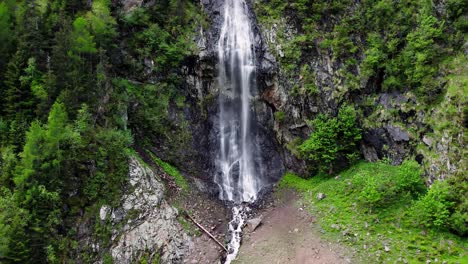 Reveal-of-a-waterfall-and-a-valley-below-with-trees,-grass-and-rocks