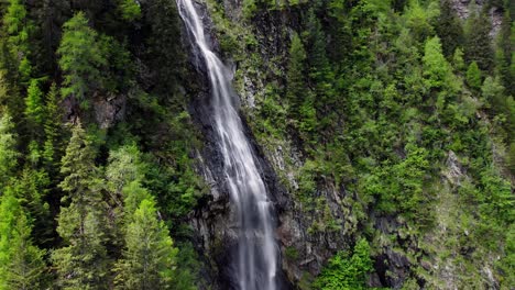 Pull-back-and-reveal-of-a-waterfall-and-trees-in-a-lush-meadow,-aerial
