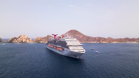 Eine-Drohne-Umkreist-Das-Carnival-Panorama-Kreuzfahrtschiff,-Das-In-Der-Bucht-Von-Cabo-San-Lucas,-Mexiko,-Vor-Anker-Liegt