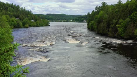 Slow-aerial-dolly-right-with-tree-in-the-foreground-moving-out-of-frame-to-reveal-rapids-on-the-Gatineau-River-in-Wakefield-Quebec-Canada