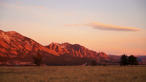 Stunning-deep-orange-pink-sunrise-sunset-Colorado-University-Boulder-Flat-irons-late-fall-winter-dead-yellow-grass-snow-on-red-rocks-peaks-early-morning-pan-to-the-left-slow-motion