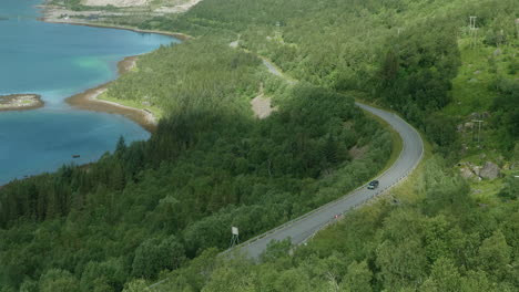Un-Automóvil-Solitario-Conduciendo-Por-Una-Hermosa-Carretera-En-Un-Paisaje-De-Fiordos-En-El-Norte-De-Noruega,-Isla-Senja,-Poco-Tráfico-En-Un-Día-Soleado-De-Verano