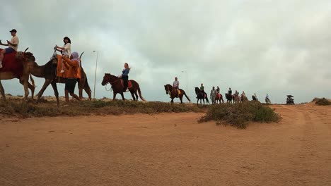 Caravana-De-Camellos-A-Caballo-Y-Dromedarios-Con-Turistas-Montando-A-Caballo-Cruzando-El-Desierto-En-Túnez