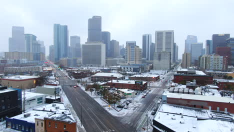 Aerial-cinematic-drone-downtown-Denver-Colorado-city-buildings-snowing-freezing-cold-winter-day-gray-bird-dramatic-city-landscape-car-traffic-passing-cross-intersection-forward-movement