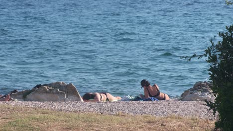 Sheltered-with-a-few-rocks-on-a-pebbled-beach-two-women-sunbathing-on-Adriatic,-Zadar,-Croatia