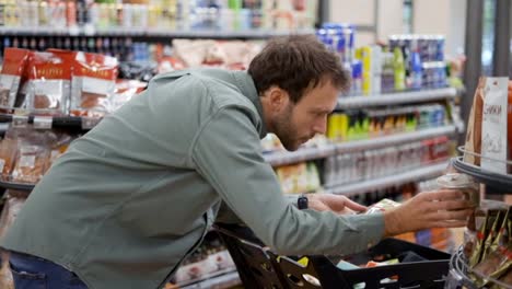 Young-man-is-selecting-cookies-in-supermarket.-He-comparing-trademarks,-prices,-reading-labels-and-ingredients.-Close-up