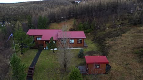 Aerial-Drone-Reveals-Kirkjufellfoss-Forest-Landscape-in-Iceland,-Panoramic-View-above-Woods,-Greenery-and-Red-Houses,-Establishing-Shot