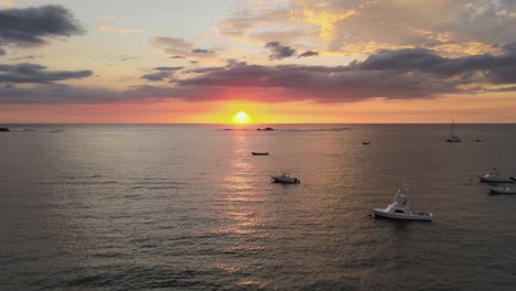 Leuchtend-Orangefarbener-Sonnenuntergang-über-Dem-Meereshorizont-Mit-Wolkengebilde-Und-Spiegelung-Auf-Dem-Wasser-Mit-Booten,-4K-Drohne-In-Costa-Rica-Dämmerung