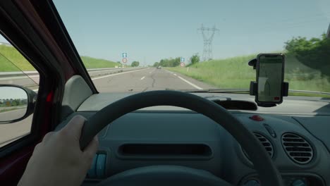 Manos-Del-Conductor-En-El-Volante-Conduciendo-Un-Coche,-Navegación-Por-Teléfono-Gps-En-La-Carretera-Soleada-En-El-Campo-En-Verano