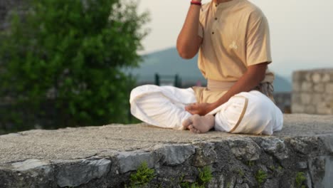 Push-in-Aufnahme-Eines-Indischen-Mannes,-Der-Auf-Einem-Stein-Sitzt-Und-Im-Morgenlicht-Bei-Sonnenaufgang-Meditiert-Und-Nadhi-Shuddhi-Macht