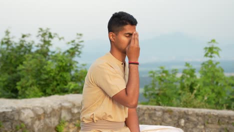 deeply-focused-young-Indian-male-meditating-in-hatha-yoga-pose-with-sun-reflecting-on-his-brown-skin-at-sunrise-in-hearth-of-nature-on-top-of-the-hill