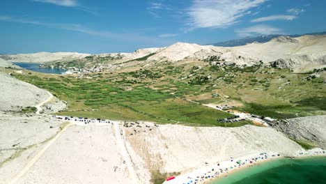 Barren-moon-like-landscape-with-green-valley,-blue-sea-and-sky-and-green-waters-at-the-beach-in-Metajna,-Pag-island,-Croatia-in-summer-and-from-above