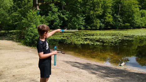 4K-60FPS-Caucasian-Boy-is-Blowing-Soap-Bubbles-at-a-Forest-Lake-in-Denmark,-Europe