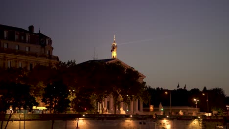 Eiffel-Tower-seen-behind-Palais-Bourbon-the-house-of-the-French-National-Assembly-at-night,-View-from-boat-on-Seine-river