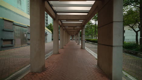Forward-wide-shot-of-empty-covered-walkway-with-trees-nearby-on-bright-day