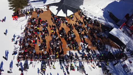 Drone-Top-view-showing-crowd-of-people-resting-and-drinking-alcohol-on-mountain-bar-after-skiing-day