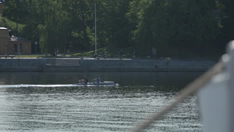 Two-people-row-a-kayak-in-calm-water-in-Stockholm,-tracking-shot