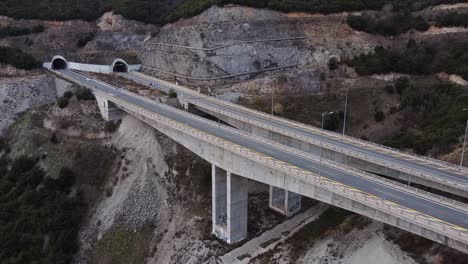 Vista-Aérea-De-Autos-En-La-Carretera-Del-Puente-En-La-Montaña-Griega-Con-Túnel-Durante-El-Atardecer-En-Grecia