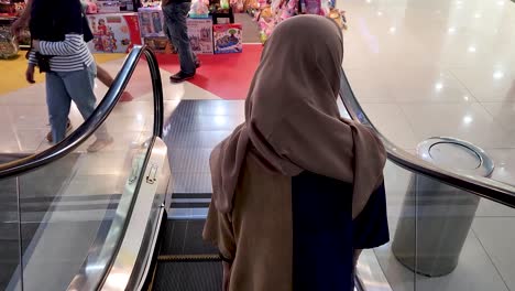Veiled-woman-moving-down-on-mall-staircase,-back-view